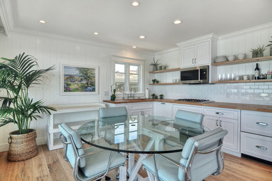 Example of a mid-sized beach style l-shaped medium tone wood floor and brown floor eat-in kitchen design in Orange County with shaker cabinets, white cabinets, wood countertops, white backsplash, subway tile backsplash, stainless steel appliances and no island