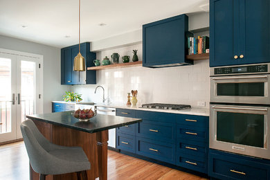 Eat-in kitchen - eclectic medium tone wood floor eat-in kitchen idea in Philadelphia with a farmhouse sink, shaker cabinets, blue cabinets, quartz countertops, white backsplash, ceramic backsplash, stainless steel appliances and an island