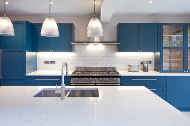 Photo of a medium sized contemporary single-wall kitchen/diner in London with a double-bowl sink, shaker cabinets, blue cabinets, granite worktops, ceramic splashback, stainless steel appliances, an island and white worktops.