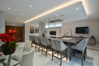 This is an example of an expansive modern single-wall kitchen/diner in Buckinghamshire with a built-in sink, flat-panel cabinets, quartz worktops, stainless steel appliances, an island and white worktops.