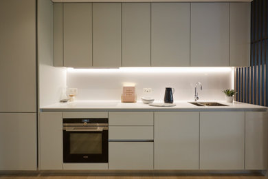 Photo of a contemporary single-wall open plan kitchen in London with a built-in sink, flat-panel cabinets, grey cabinets, engineered stone countertops, white appliances, no island and white worktops.