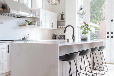 Scandi l-shaped kitchen in Vancouver with a submerged sink, shaker cabinets, white cabinets, engineered stone countertops, white splashback, stainless steel appliances, light hardwood flooring, an island and white worktops.