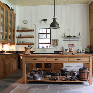 This is an example of a large farmhouse l-shaped kitchen/diner in New York with a double-bowl sink, beaded cabinets, medium wood cabinets, soapstone worktops, black splashback, slate flooring and an island.
