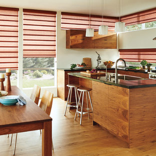Photo of a large modern l-shaped eat-in kitchen in Orange County with a drop-in sink, flat-panel cabinets, medium wood cabinets, granite benchtops, panelled appliances, medium hardwood floors and with island.