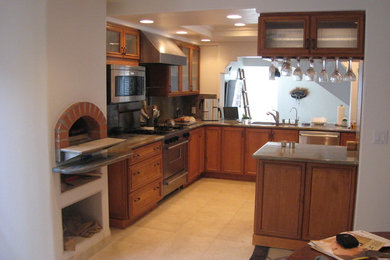 Tuscan l-shaped ceramic tile eat-in kitchen photo in Orange County with a drop-in sink, glass-front cabinets, medium tone wood cabinets, granite countertops, gray backsplash, ceramic backsplash, stainless steel appliances and a peninsula