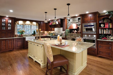 Inspiration for a timeless l-shaped light wood floor eat-in kitchen remodel in New York with an island, a farmhouse sink, raised-panel cabinets, dark wood cabinets, granite countertops, beige backsplash, stone tile backsplash and stainless steel appliances