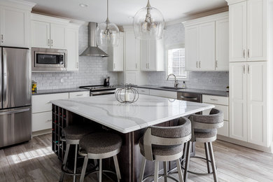 Mid-sized transitional l-shaped ceramic tile and gray floor kitchen photo in Other with an undermount sink, shaker cabinets, white cabinets, quartz countertops, white backsplash, marble backsplash, stainless steel appliances, an island and gray countertops