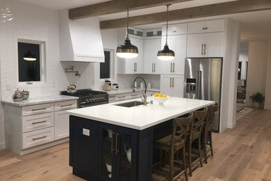 Inspiration for a large farmhouse l-shaped medium tone wood floor and brown floor kitchen remodel in Los Angeles with an undermount sink, shaker cabinets, white cabinets, solid surface countertops, white backsplash, ceramic backsplash, stainless steel appliances and an island