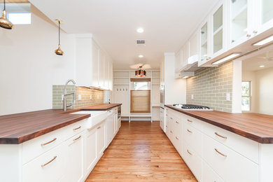 Eat-in kitchen - mid-sized contemporary galley medium tone wood floor eat-in kitchen idea in Austin with a farmhouse sink, recessed-panel cabinets, white cabinets, wood countertops, green backsplash, porcelain backsplash, white appliances and a peninsula