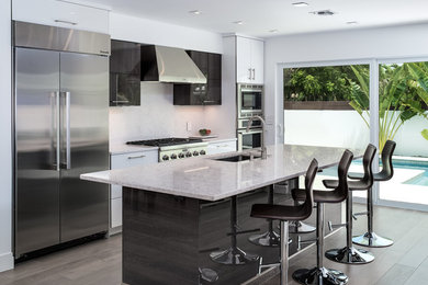 Example of a mid-sized beach style medium tone wood floor kitchen design in Miami with a single-bowl sink, flat-panel cabinets, quartz countertops, white backsplash, stone slab backsplash, stainless steel appliances and an island