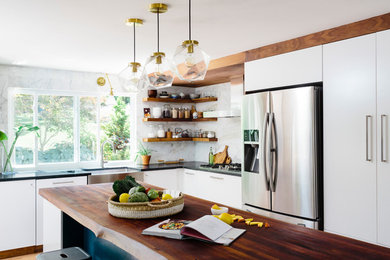 Contemporary l-shaped kitchen in Boston with a belfast sink, flat-panel cabinets, white cabinets, wood worktops, white splashback, stainless steel appliances, medium hardwood flooring, an island, brown floors and black worktops.