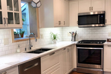 Example of a mid-sized classic l-shaped medium tone wood floor and brown floor enclosed kitchen design in New York with a double-bowl sink, recessed-panel cabinets, white cabinets, quartz countertops, white backsplash, ceramic backsplash, stainless steel appliances, no island and white countertops