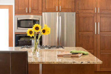 Cette photo montre une cuisine américaine chic avec des portes de placard marrons, un plan de travail en granite, un électroménager en acier inoxydable, un sol en bois brun et îlot.