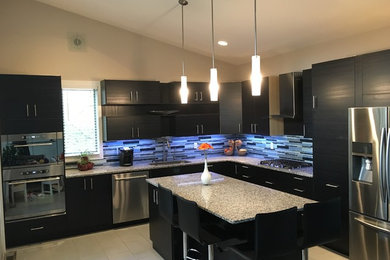 Photo of a medium sized contemporary l-shaped kitchen/diner in New York with a single-bowl sink, flat-panel cabinets, dark wood cabinets, granite worktops, blue splashback, glass tiled splashback, stainless steel appliances, ceramic flooring and an island.
