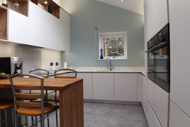 This is an example of a large modern u-shaped kitchen/diner in Other with a submerged sink, flat-panel cabinets, white cabinets, onyx worktops, white splashback, black appliances, lino flooring, an island, grey floors and white worktops.