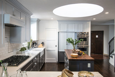 Kitchen - traditional l-shaped dark wood floor kitchen idea in Los Angeles with a farmhouse sink, recessed-panel cabinets, blue cabinets, white backsplash, subway tile backsplash, paneled appliances and an island