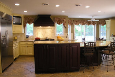 Example of a large classic l-shaped ceramic tile kitchen pantry design in New York with an island, raised-panel cabinets, yellow cabinets, granite countertops, beige backsplash, ceramic backsplash, stainless steel appliances and a double-bowl sink