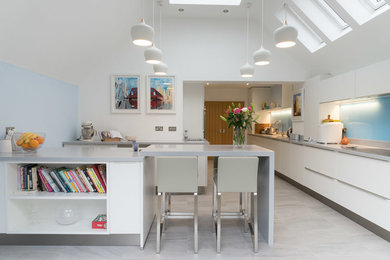 Photo of a large contemporary l-shaped kitchen/diner in Berkshire with flat-panel cabinets, white cabinets, composite countertops, blue splashback, glass sheet splashback, stainless steel appliances, porcelain flooring and a breakfast bar.