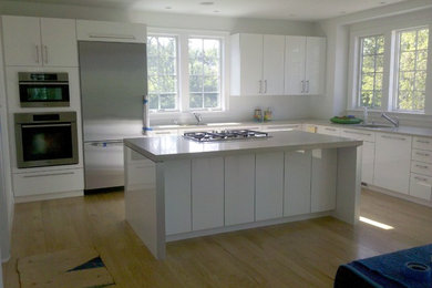 Inspiration for a large modern l-shaped light wood floor and beige floor kitchen remodel in Boston with an undermount sink, flat-panel cabinets, white cabinets, solid surface countertops, stainless steel appliances and an island