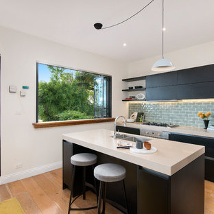 Photo of a contemporary single-wall kitchen in Sydney with a double-bowl sink, flat-panel cabinets, black cabinets, subway tile splashback, stainless steel appliances, medium hardwood floors, with island, brown floor, solid surface benchtops, grey splashback and white benchtop.