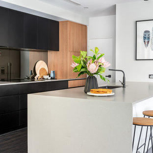 Photo of a contemporary kitchen in Perth with an undermount sink, black cabinets, quartz benchtops, laminate floors, grey benchtop, flat-panel cabinets, grey splashback, glass sheet splashback, stainless steel appliances, a peninsula and black floor.