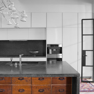 Idee per una grande cucina industriale con lavello sottopiano, ante lisce, ante bianche, parquet chiaro, isola, top in pietra calcarea, paraspruzzi nero e elettrodomestici da incasso