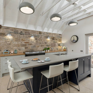 Photo of a large industrial eat-in kitchen in Edinburgh with an integrated sink, flat-panel cabinets, travertine floors, with island, blue cabinets and wood benchtops.