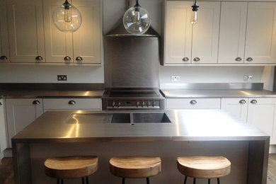 This is an example of a medium sized urban l-shaped kitchen/diner in Other with a built-in sink, white cabinets, stainless steel worktops, metal splashback and an island.