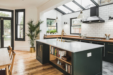 Large urban galley cement tile floor and gray floor eat-in kitchen photo in London with an undermount sink, shaker cabinets, green cabinets, wood countertops, white backsplash, subway tile backsplash and an island