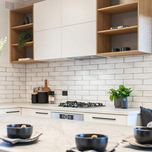 Cette image montre une grand cuisine américaine design en U avec un évier 2 bacs, un placard à porte plane, des portes de placard blanches, un plan de travail en quartz modifié, une crédence blanche, une crédence en carrelage métro, un électroménager noir, un sol en bois clair, un îlot central, un sol jaune et un plan de travail gris.