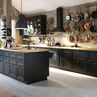 Inspiration for a mid-sized industrial galley medium tone wood floor and gray floor eat-in kitchen remodel in Columbus with a drop-in sink, recessed-panel cabinets, black cabinets, wood countertops, brown backsplash, brick backsplash, black appliances, an island and brown countertops