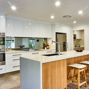 Photo of a mid-sized contemporary galley open plan kitchen in Gold Coast - Tweed with an undermount sink, flat-panel cabinets, white cabinets, mirror splashback, stainless steel appliances, with island, beige floor, white benchtop, quartz benchtops and metallic splashback.