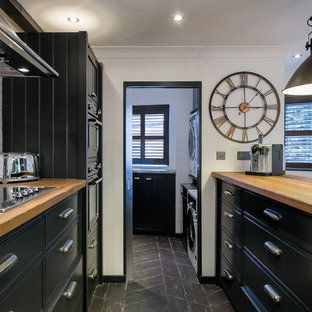 Inspiration for an industrial galley kitchen in London with flat-panel cabinets, black cabinets, wood worktops, white splashback, integrated appliances, an island, black floors and brown worktops.