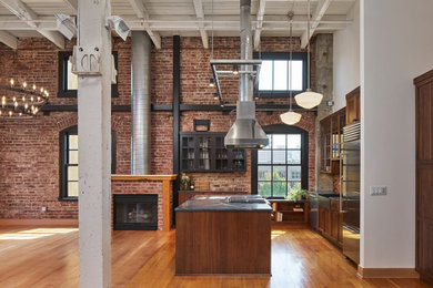 Mid-sized urban l-shaped medium tone wood floor, brown floor and exposed beam open concept kitchen photo in Portland with a farmhouse sink, glass-front cabinets, dark wood cabinets, soapstone countertops, multicolored backsplash, ceramic backsplash, stainless steel appliances, an island and black countertops