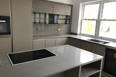 Design ideas for a medium sized urban l-shaped kitchen/diner in Buckinghamshire with an integrated sink, flat-panel cabinets, light wood cabinets, quartz worktops, grey splashback, an island and grey worktops.