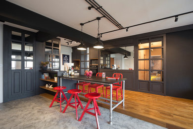 Cette image montre une cuisine urbaine avec des portes de placard grises, un électroménager noir, un sol en bois brun et une péninsule.