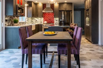 Mid-sized urban l-shaped ceramic tile and gray floor kitchen photo in Boston with a farmhouse sink, shaker cabinets, gray cabinets, solid surface countertops, red backsplash, glass tile backsplash, stainless steel appliances, an island and multicolored countertops