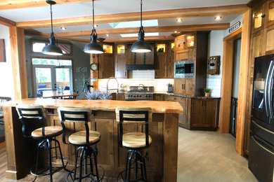 Inspiration for a large industrial l-shaped light wood floor and brown floor eat-in kitchen remodel in Vancouver with a farmhouse sink, shaker cabinets, medium tone wood cabinets, white backsplash, subway tile backsplash, stainless steel appliances, an island and black countertops