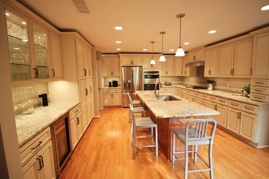 Elegant u-shaped medium tone wood floor eat-in kitchen photo in Indianapolis with an undermount sink, raised-panel cabinets, beige cabinets, granite countertops, multicolored backsplash, glass tile backsplash, stainless steel appliances and an island