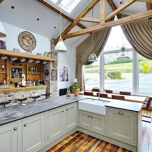 Photo of a large rustic open plan kitchen in Other with shaker cabinets, green cabinets, wood splashback, light hardwood flooring, an island, beige floors and grey worktops.