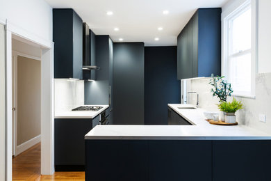 Example of a mid-sized minimalist galley medium tone wood floor and brown floor eat-in kitchen design in San Francisco with an undermount sink, flat-panel cabinets, black cabinets, quartz countertops, white backsplash, quartz backsplash, stainless steel appliances, a peninsula and white countertops