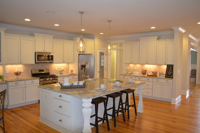 Example of a large transitional galley medium tone wood floor and beige floor eat-in kitchen design in Raleigh with a farmhouse sink, shaker cabinets, beige cabinets, granite countertops, beige backsplash, stone tile backsplash, stainless steel appliances and an island