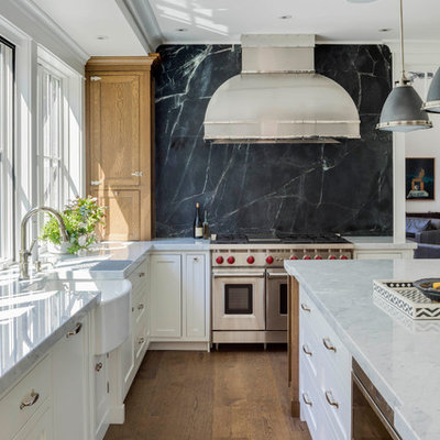 Kitchen - large traditional l-shaped medium tone wood floor and brown floor kitchen idea in Boston with a farmhouse sink, shaker cabinets, white cabinets, marble countertops, black backsplash, stone slab backsplash, stainless steel appliances, an island and white countertops