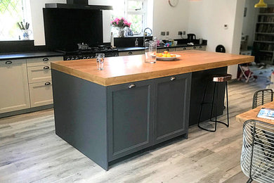 Photo of a medium sized classic l-shaped kitchen/diner in Surrey with a submerged sink, shaker cabinets, grey cabinets, quartz worktops, black splashback, black appliances, laminate floors, an island, grey floors and black worktops.