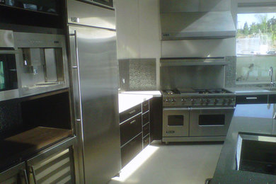 Ejemplo de cocina moderna grande con armarios con paneles lisos, puertas de armario de madera en tonos medios, encimera de acrílico, salpicadero metalizado, electrodomésticos de acero inoxidable y una isla