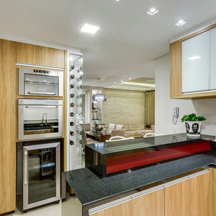 Photo of a mid-sized contemporary u-shaped open plan kitchen in Other with a double-bowl sink, flat-panel cabinets, light wood cabinets, granite benchtops, white splashback, ceramic splashback, stainless steel appliances, porcelain floors and a peninsula.