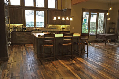 Inspiration for a large rustic l-shaped kitchen in Boise with a belfast sink, shaker cabinets, dark wood cabinets, grey splashback, metro tiled splashback, stainless steel appliances, medium hardwood flooring, an island and brown floors.