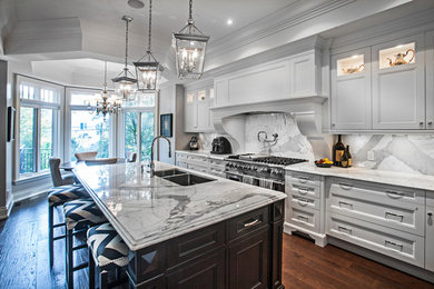 Example of a large classic l-shaped dark wood floor and brown floor kitchen design in Toronto with an undermount sink, shaker cabinets, white cabinets, marble countertops, white backsplash, marble backsplash, stainless steel appliances and an island