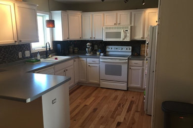 Example of a small transitional u-shaped light wood floor eat-in kitchen design in Other with white cabinets, a peninsula, a double-bowl sink, shaker cabinets, laminate countertops, blue backsplash, mosaic tile backsplash and white appliances