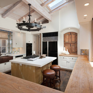 Southwestern kitchen inspiration - Inspiration for a southwestern galley dark wood floor kitchen remodel in San Diego with a farmhouse sink, raised-panel cabinets, white cabinets, multicolored backsplash, black appliances and an island